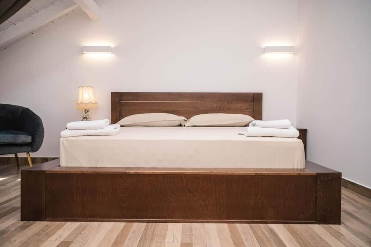 A modern bed with a wooden headboard, two bedside lamps, and a chair.