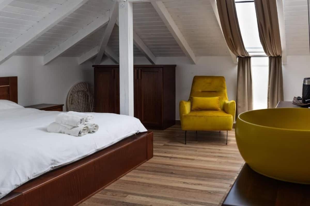 A bedroom with a bed, a yellow armchair, a large bowl, and wooden flooring.