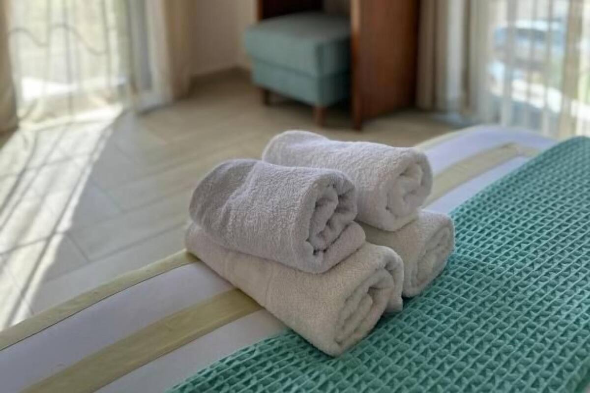 A hotel room with a bed, a green textured area rug, a wooden nightstand with a mirror, and a window with curtains.