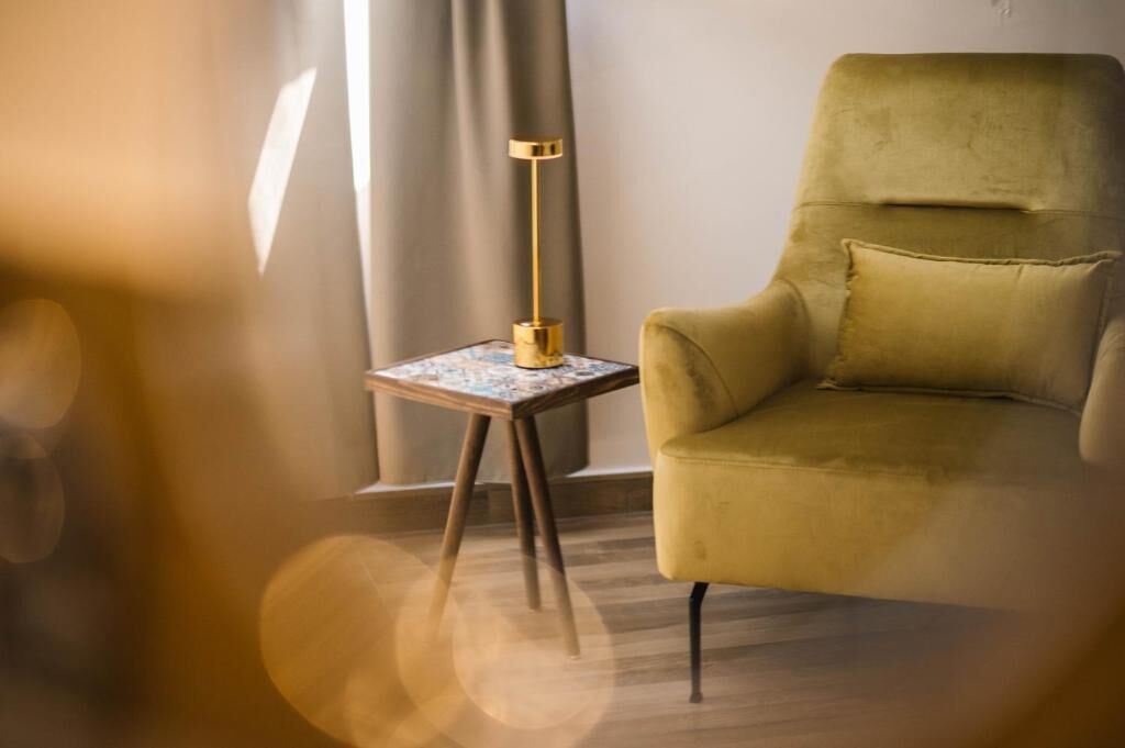 A room with a yellow armchair, a small table with a lamp, and a window with curtains.