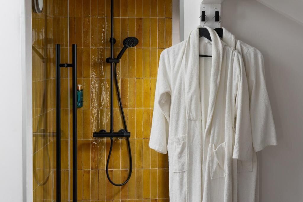 A bathroom with a shower, a towel rack with a white bathrobe, and a bottle of shampoo.