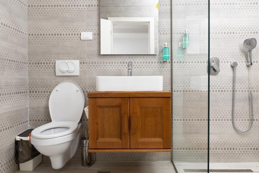 Un baño con inodoro, lavabo, armario de madera, espejo, ducha y baldosas estampadas.