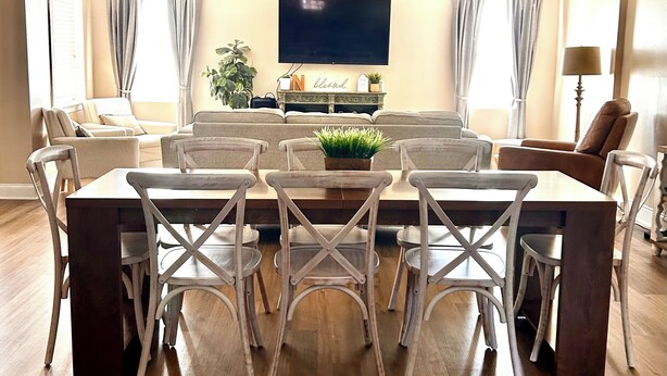 A dining area with a wooden table and white chairs, a TV mounted on the wall, and a plant on the sideboard. - Spacious 4-bedroom house in tranquil Grovetown (Grovetown)