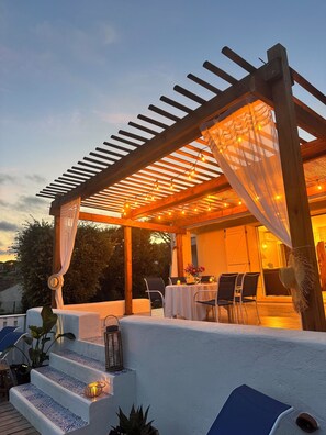 A covered outdoor seating area with tables and chairs, a pergola with string lights, and a staircase with patterned tiles. - Provencal Villa near the beach  ( 7 minutes walking) (Roquebrune-sur-Argens)