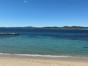 Ein Strand mit klarem Wasser, einer Mole und sanft abfallenden Hügeln im Hintergrund.