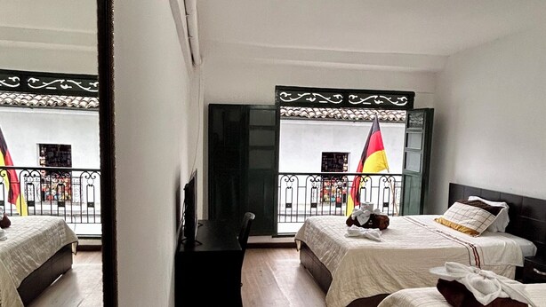 A hotel room with three beds, a large mirror, and a view of the street. - Hotel Santa Marta's (Popayán)