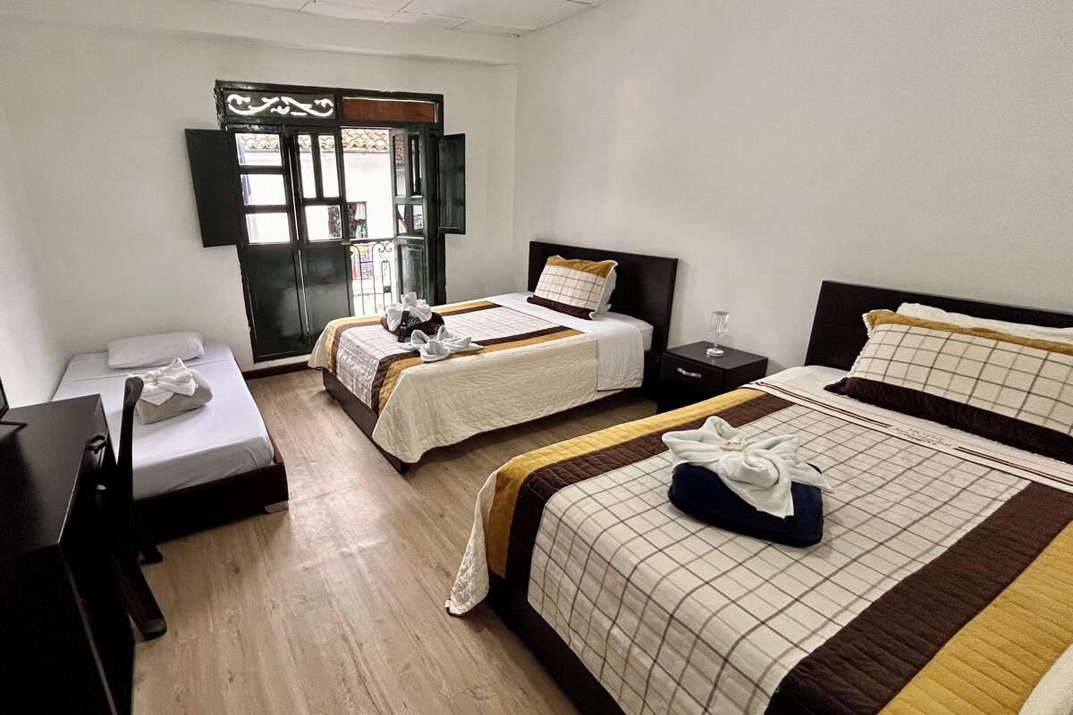 Habitación de hotel con dos camas, un escritorio, una silla, un televisor y ventana con vistas.