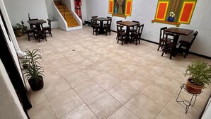 Un'ampia area interna con pavimento piastrellato, diversi tavoli e sedie in legno, una scala e un'ampia finestra con vista.