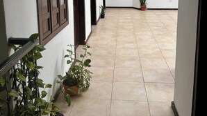A corridor with tiled flooring, wooden doors, potted plants, a mounted television, and a ceiling with a skylight. - Hotel Santa Marta's (Popayán)