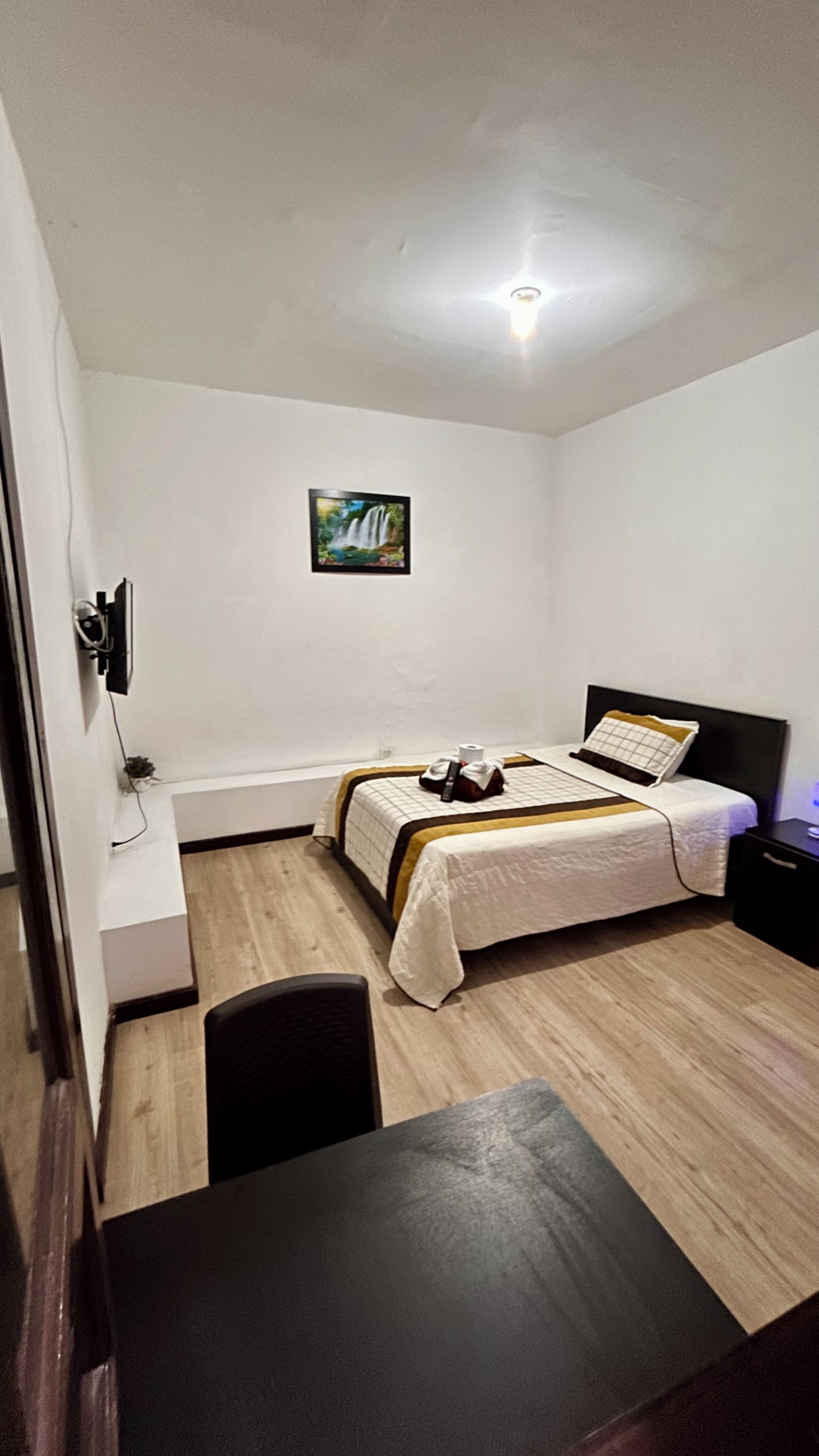 A bedroom with a bed, bedside table, and a wall-mounted TV.