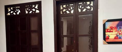 Una habitación con una puerta grande de madera, una ventana con adornos recortados y una planta en maceta.