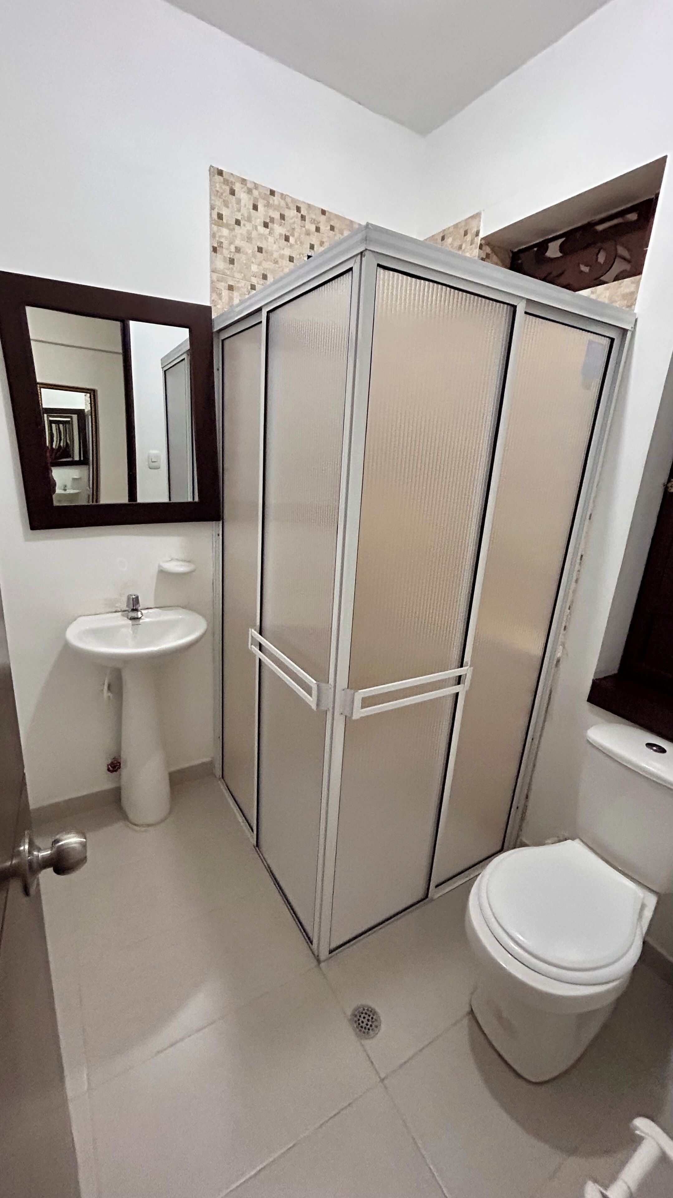 Un bagno con lavandino bianco, water e armadio specchiato con rivestimento in piastrelle.