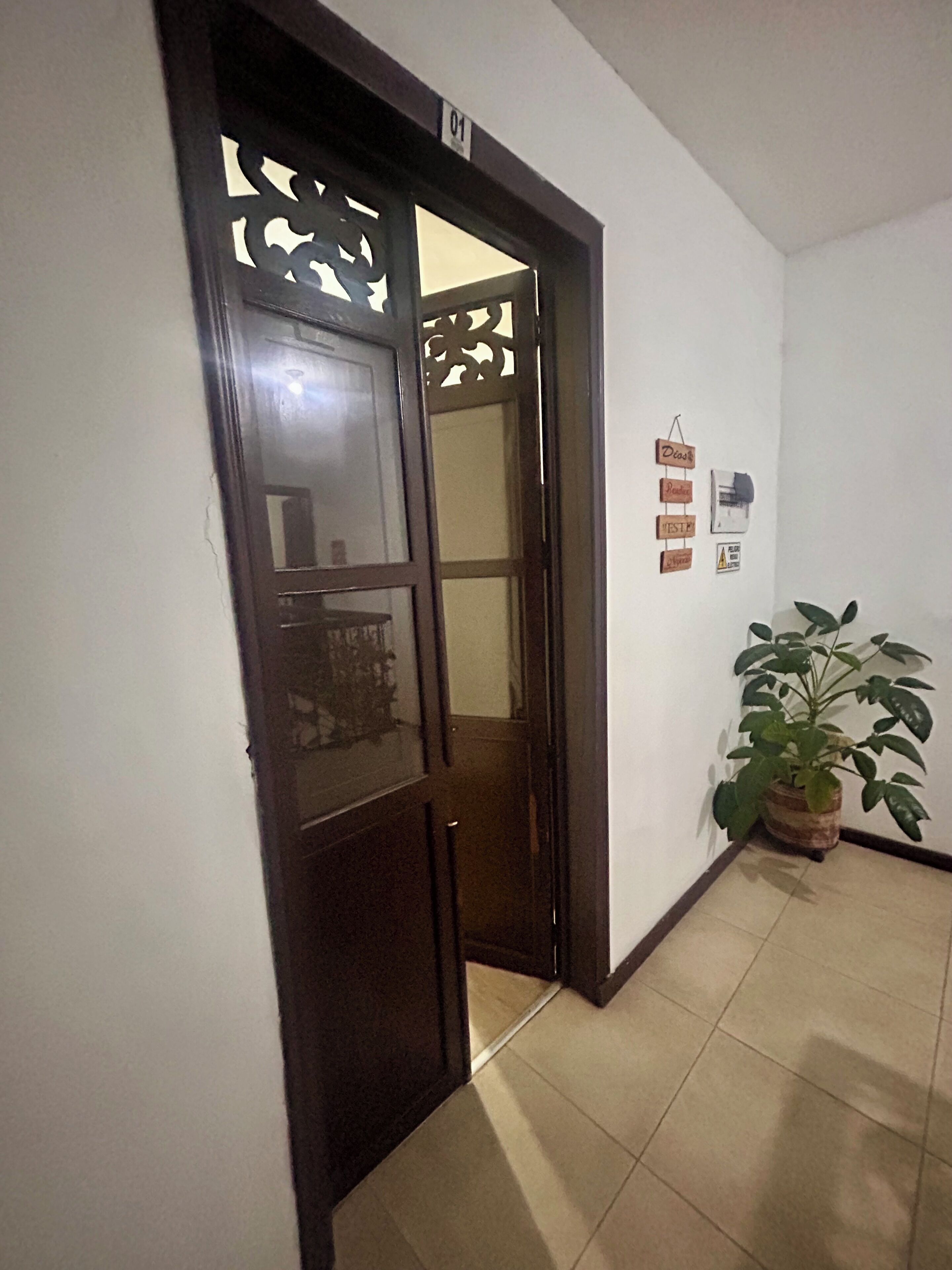 Un pasillo con una puerta de madera, una planta en maceta y una pared con un cartel.