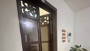 Un pasillo con una puerta de madera, una planta en maceta y una pared con un cartel.
