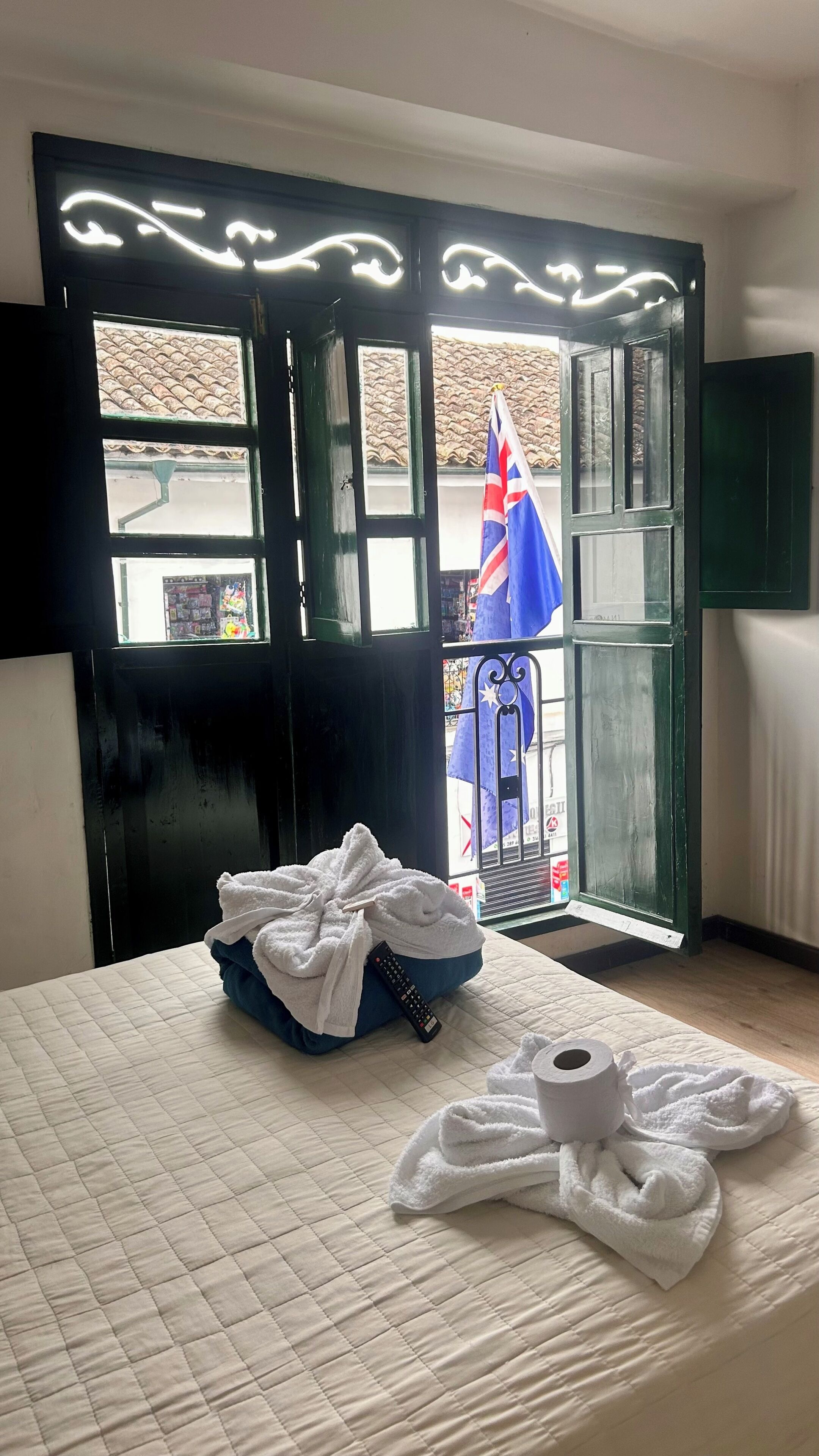 A hotel room with a bed, a window with a view of a flag, and a pile of towels on the bed.