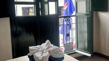 A hotel room with a bed, a window with a view of a flag, and a pile of towels on the bed.
