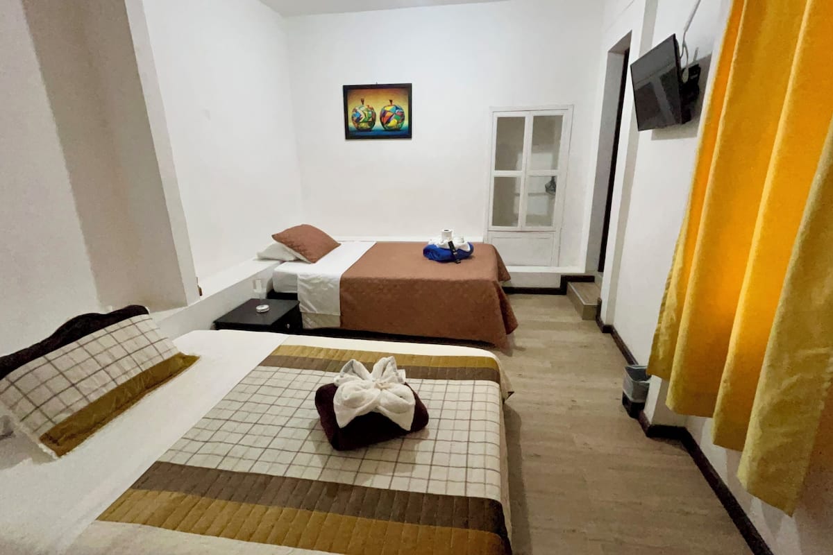 Habitación de hotel con dos camas, un televisor montado en la pared y una ventana con cortinas.