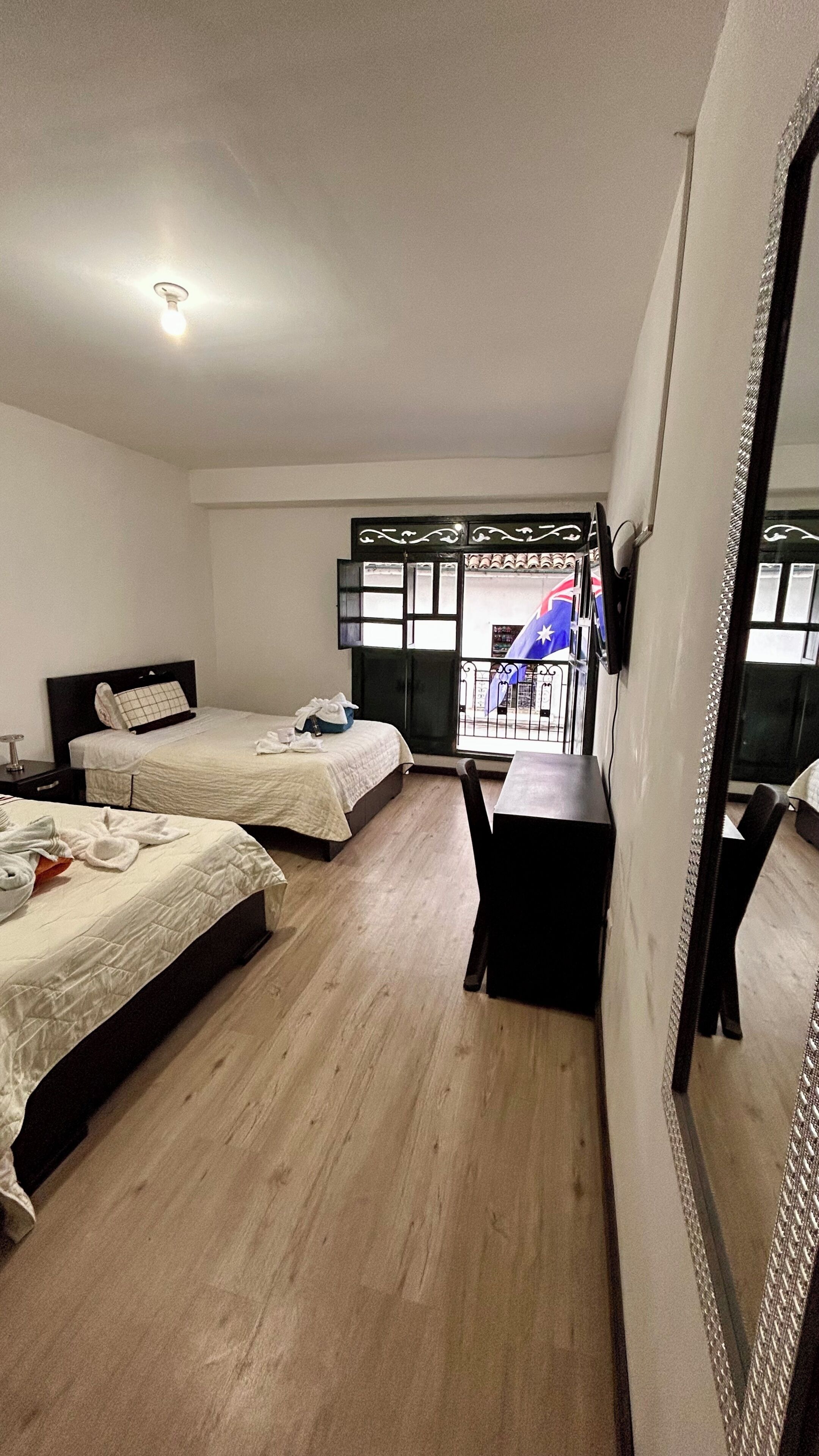 Hotellihuone, jossa on kaksi sänkyä, työpöytä, tuoli, suuri peili ja ikkuna, josta on näkymä kadulle.