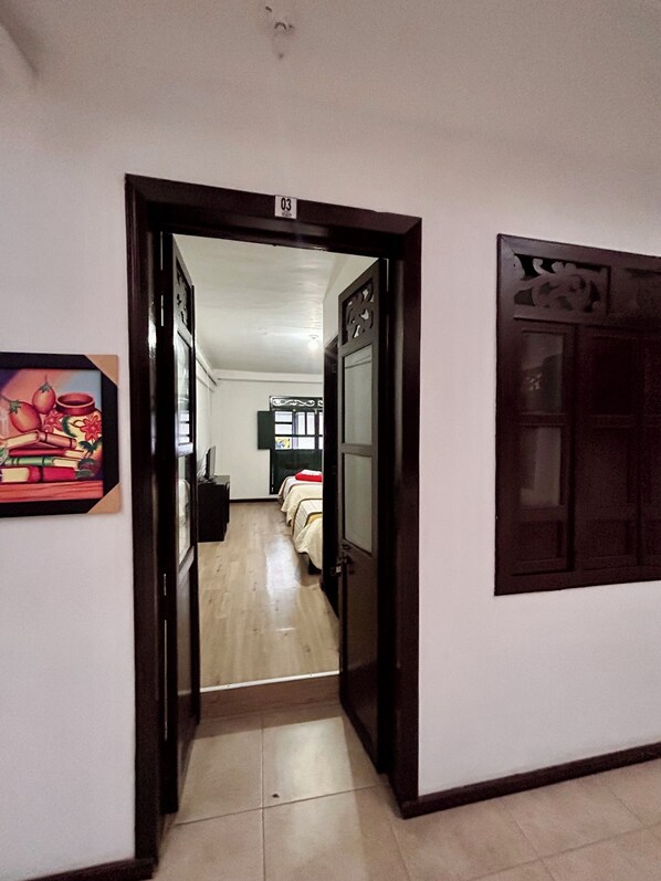 A hallway leading to a room with a bed, a door with a number, and a wall-mounted artwork. - Hotel Santa Marta's (Popayán)