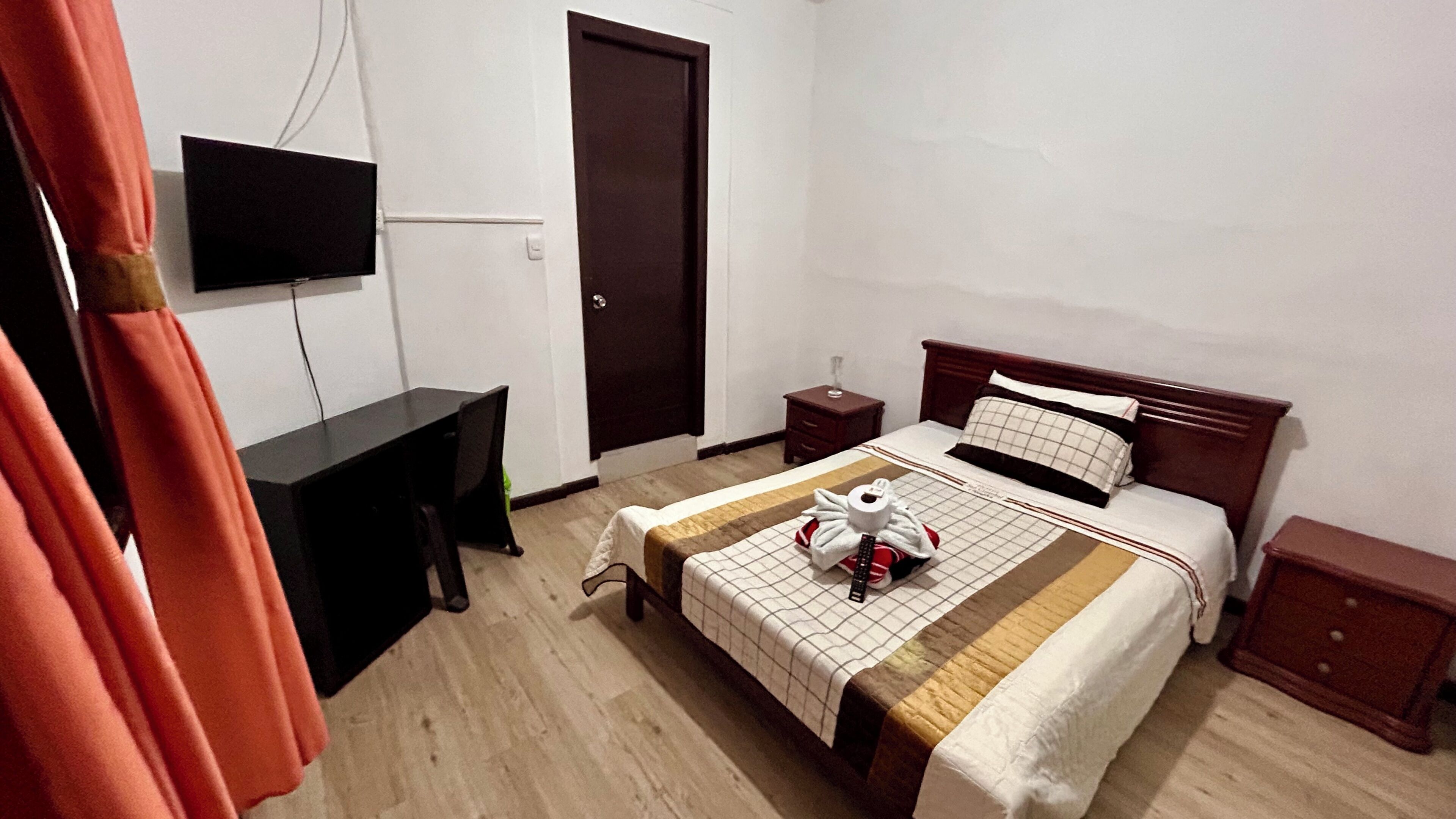 Une chambre d’hôtel comprenant un lit, une table de chevet, un bureau, un téléviseur fixé au mur et une porte.