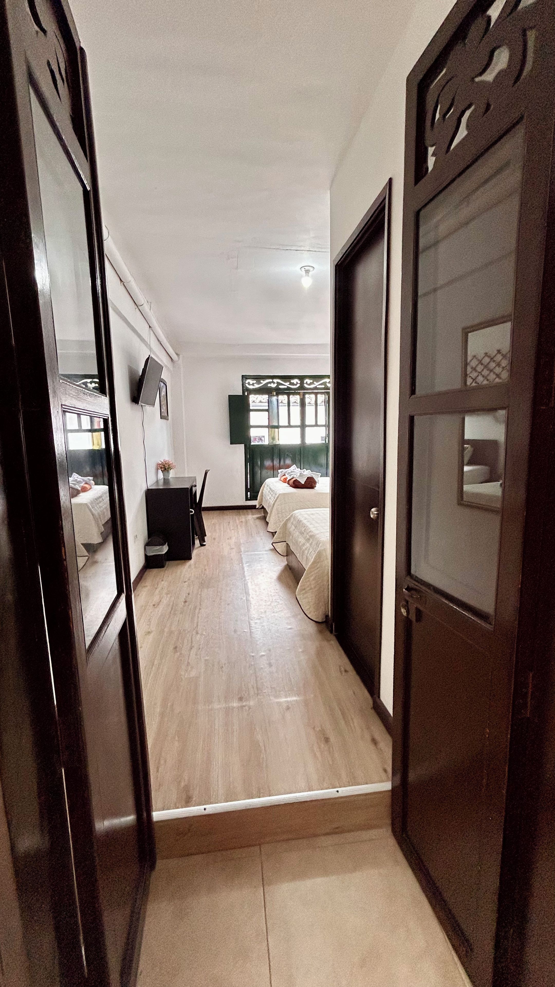 Una habitación de hotel con piso de madera, una cama, un escritorio y un ventanal con vistas.