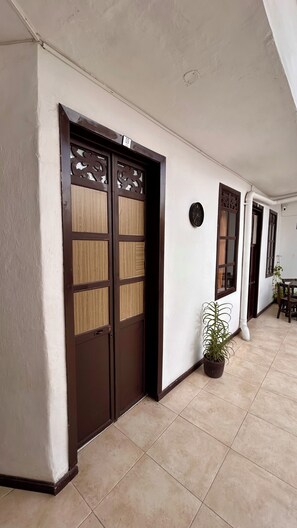 A hallway with a double wooden door, a potted plant, and a clock on the wall.