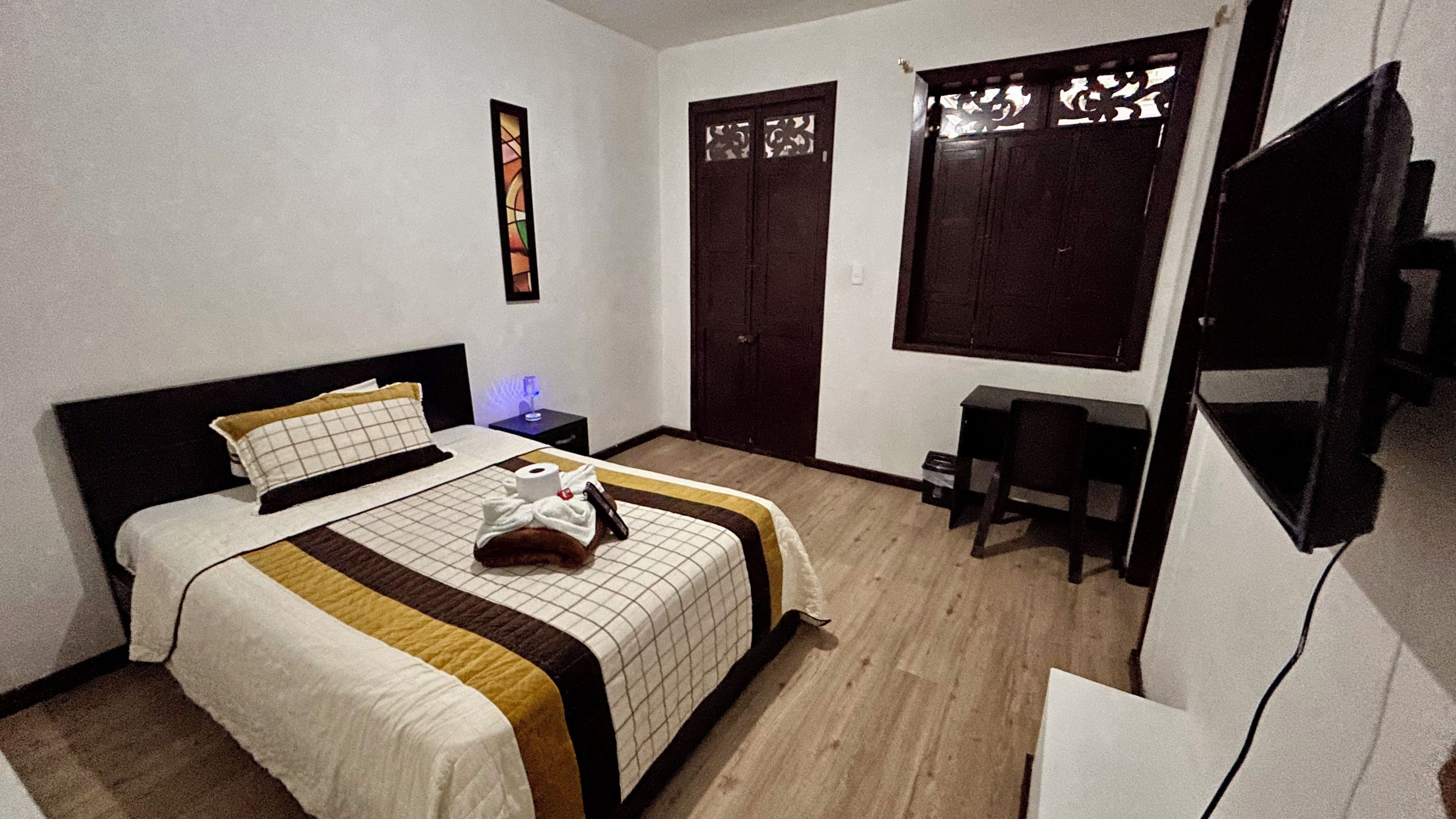 A hotel room with a bed, a desk, a chair, a wardrobe, and a television.