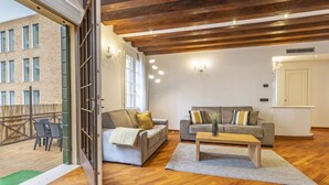 Un soggiorno open space con pavimento in legno, due divani, un tavolino da caffè e vista su un edificio attraverso una porta in vetro.