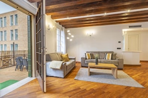 Ein offener Wohnbereich mit Holzboden, zwei Sofas, einem Couchtisch und Blick auf ein Gebäude durch eine Glastür.