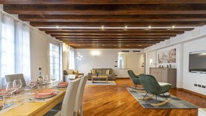Un soggiorno moderno con soffitto in legno, una zona pranzo con tavolo apparecchiato per quattro persone e un angolo cottura con televisore.