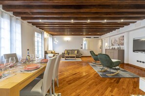 Ein modernes Wohnzimmer mit Holzboden, einer Essecke mit Tisch für vier Personen und einer Küchenzeile mit Fernseher.