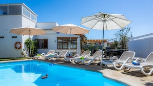 A swimming pool with lounge chairs and umbrellas, a lifebuoy, and a building with windows and a door. - Villa Luna with Pool and Mountain Views (Alcúdia)