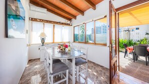A dining area with a round table, white chairs, and a window with a view of buildings. - Villa Luna with Pool and Mountain Views (Alcúdia)