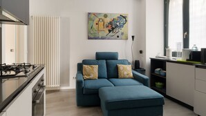 Eine moderne Küche mit Gaskochfeld, einem blauen Sofa mit gemusterten Kissen und einem großen abstrakten Gemälde an der Wand.