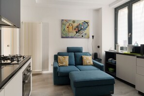 A modern kitchen with a gas stove, a blue sofa with patterned cushions, and a large abstract painting on the wall. - GuestHost - Cozy 40m2 apartment, ideal for two, on the third floor of a building with lift.The accommodation is located a stone's throw from Piazza Vetra, a historic district of Milan, located behind the Basilica of San Lorenzo, transformed from a popula (Milan)