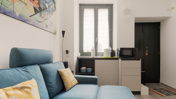 Ein modernes Wohnzimmer mit Sofa, einer kleinen Küchenzeile und einer Tür.