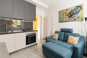 A modern kitchen with grey cabinets, a built-in oven, and a blue sofa with patterned cushions. - GuestHost - Cozy 40m2 apartment, ideal for two, on the third floor of a building with lift.The accommodation is located a stone's throw from Piazza Vetra, a historic district of Milan, located behind the Basilica of San Lorenzo, transformed from a popula (Milan)