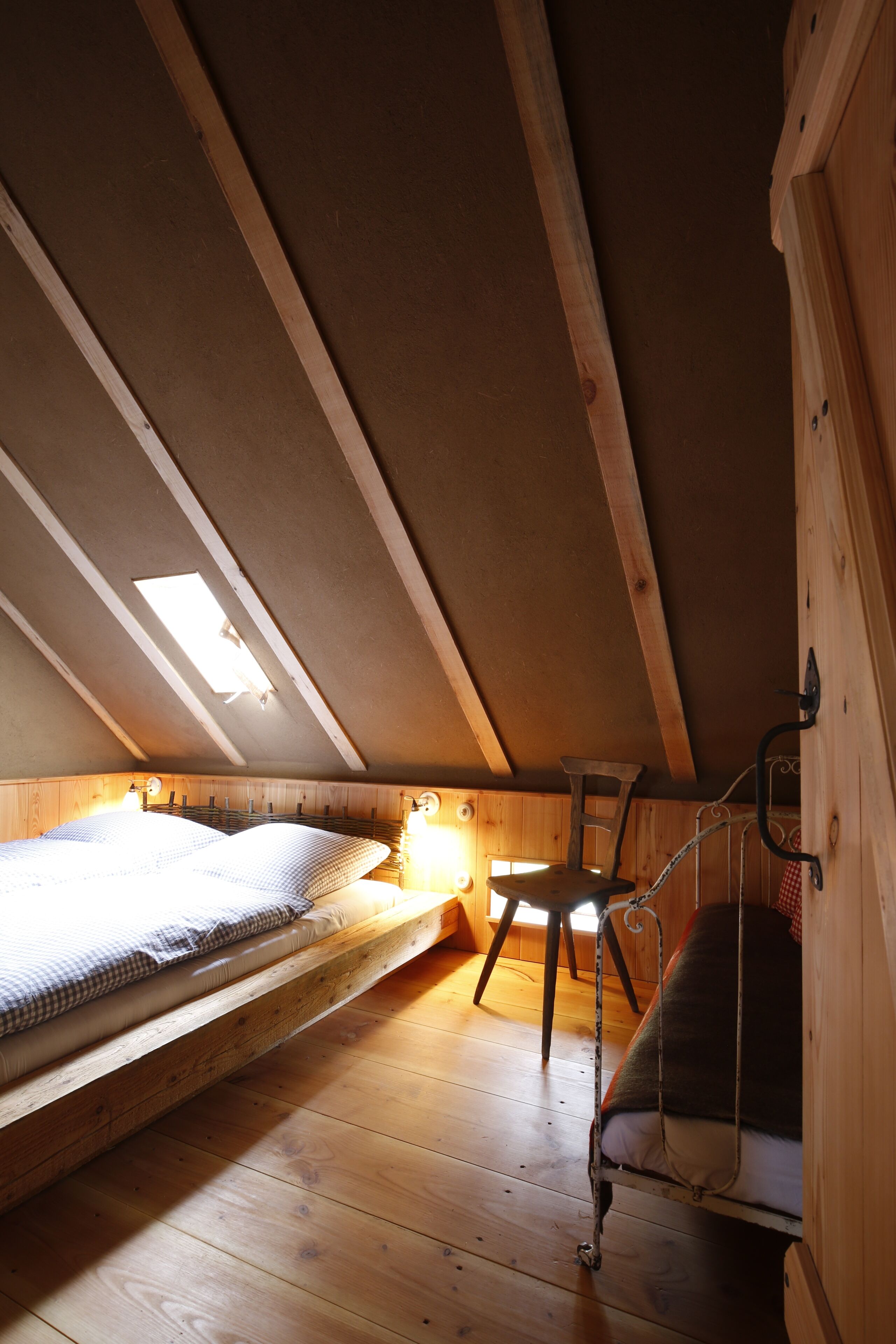 A loft bedroom with a sloped ceiling, a bunk bed, a desk, and a chair.