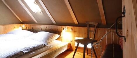A loft bedroom with a sloped ceiling, a bunk bed, a desk, and a chair.