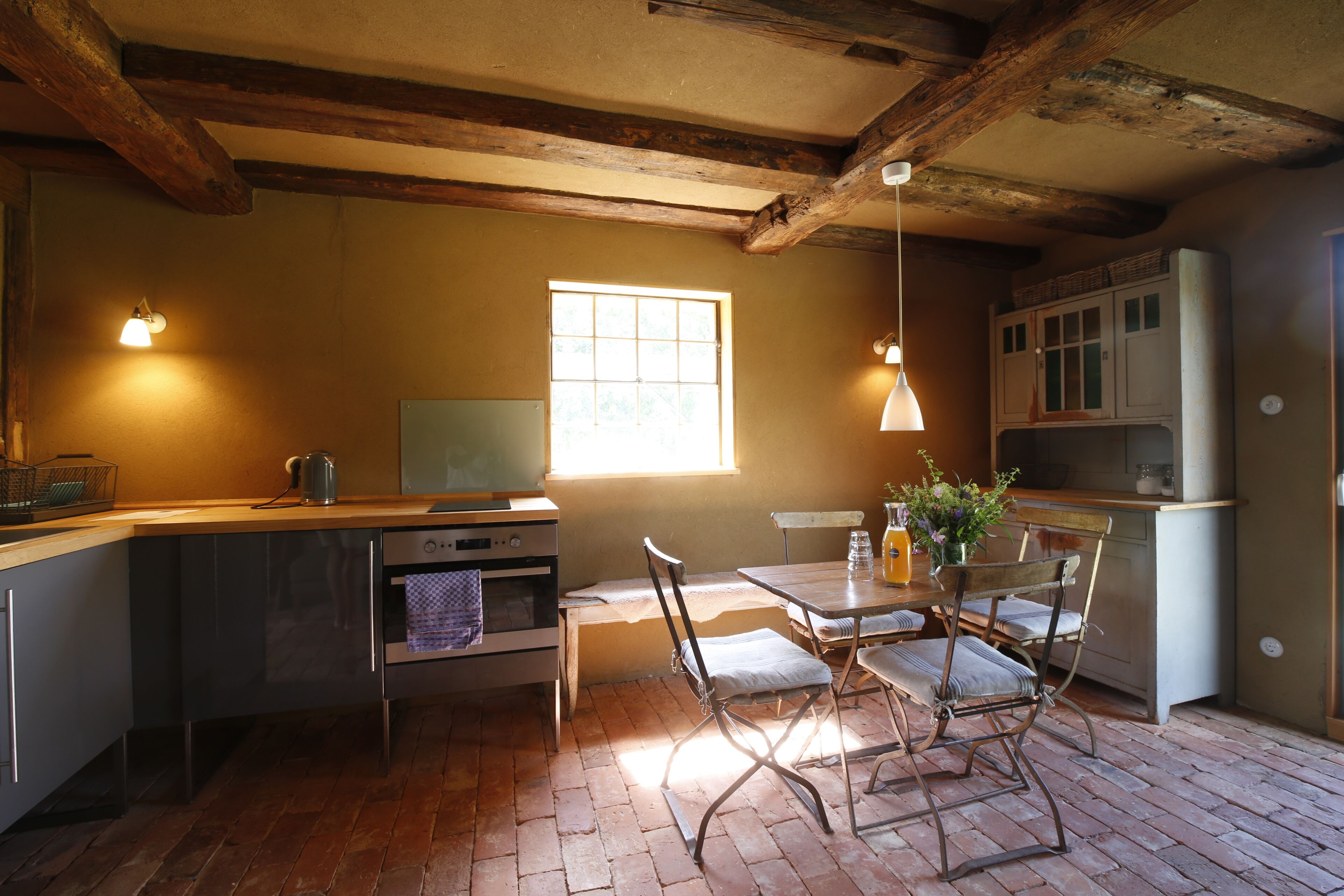 A kitchen with wooden beams, a window, a dining table with chairs, and a refrigerator.