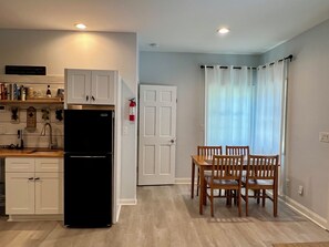 A kitchen with white cabinets, a black refrigerator, and a dining area with wooden chairs and a table. - Relaxing 1BR Oasis with Dreamy Spa Bathroom (Wilmington)