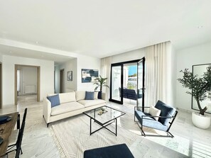 A modern living room with a sofa, armchair, coffee table, and a large sliding glass door leading to an outdoor area. - Casa Aura , Apartement In La Marsa (La Marsa)