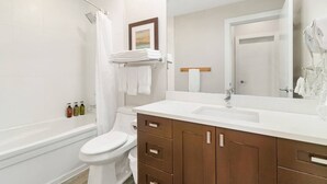 Ein modernes Badezimmer mit Toilette, Dusche, Waschtisch mit Spiegel und ordentlich gefalteten Handtüchern.