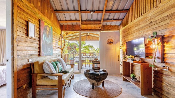 A wooden interior with a sofa, a round table, and a TV mounted on the wall.