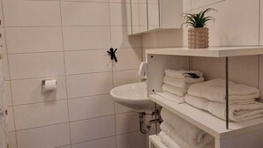 A bathroom with white tiles, a sink, a toilet, a towel rack, and a shelf with toiletries.