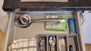 A kitchen with a stove, drawer with utensils, and a blue container on the countertop.