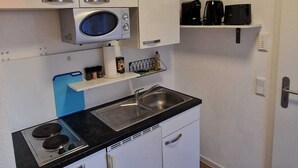 A compact kitchen with white cabinets, a built-in microwave, a stove, and a coffee maker.