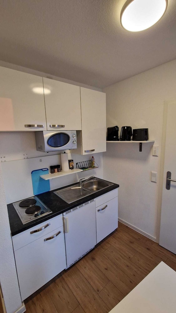 Cocina compacta con armarios blancos, microondas integrado, estufa y cafetera.
