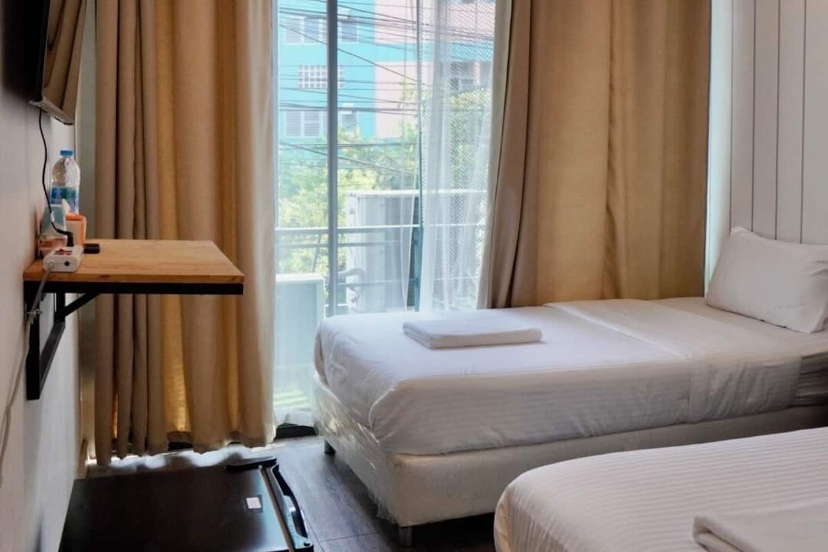 A hotel room with a bed, a small desk, and a window with curtains.