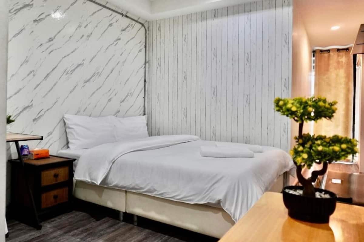 A bedroom with a bed, a nightstand, a wooden table, and a potted plant.